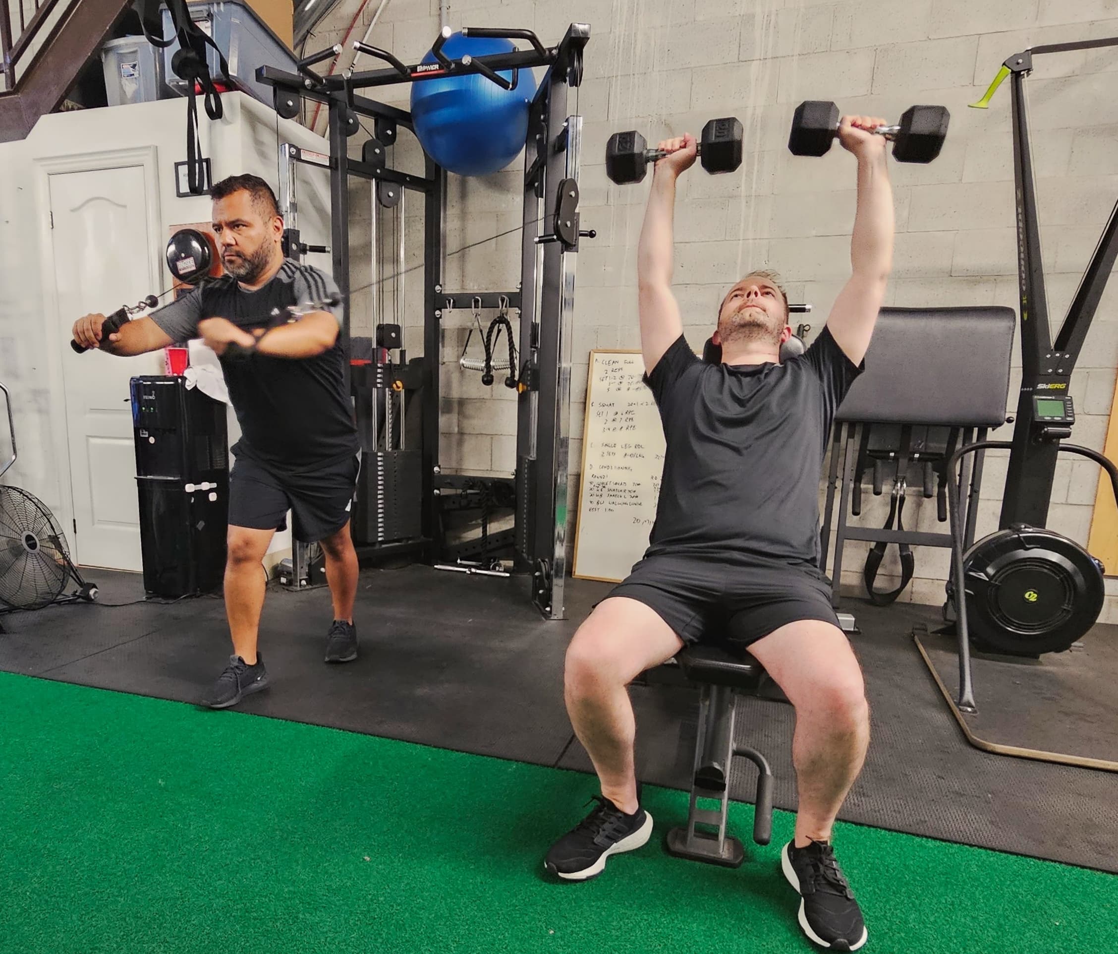 John coaching a client through seated dumbbell shoulder presses at Carpio gym